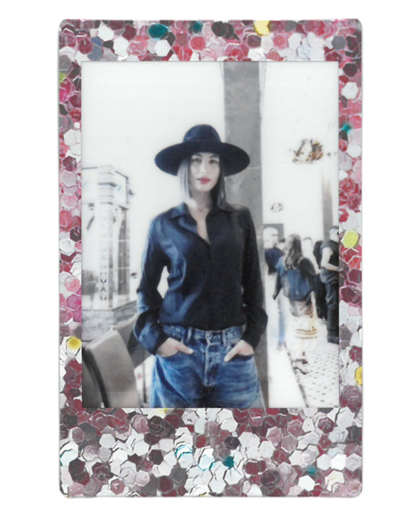 Rym saidi poses in a wide black hat and a black button up over jeans 